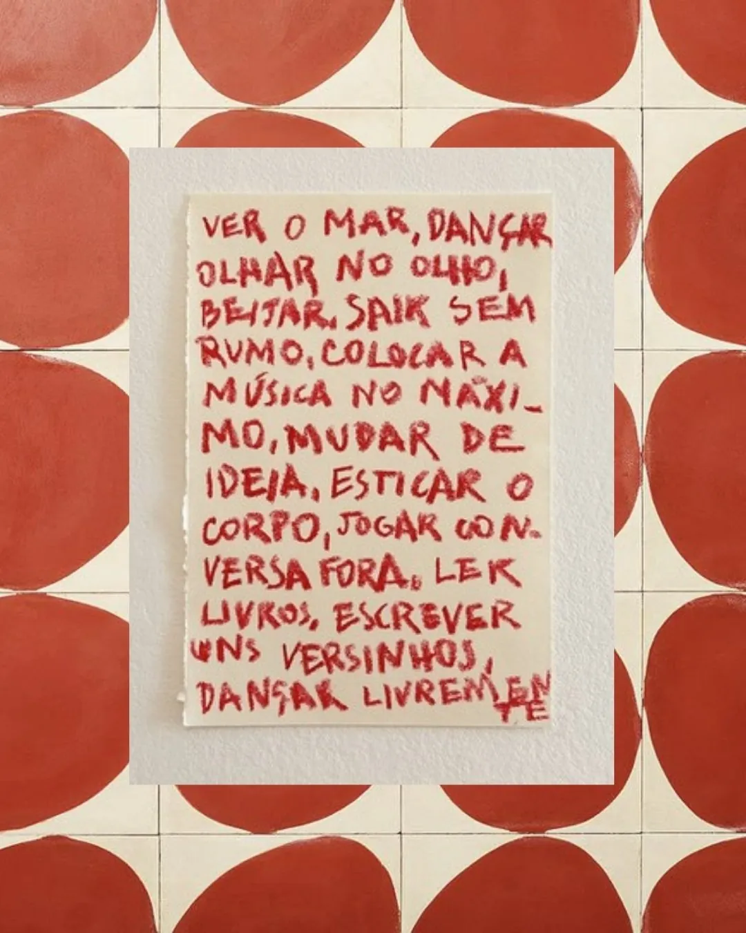 Papel com versos escritos à mão em vermelho: ver o mar, dançar, olhar no olho, beijar, sair sem rumo, colocar a música no máximo, mudar de ideia