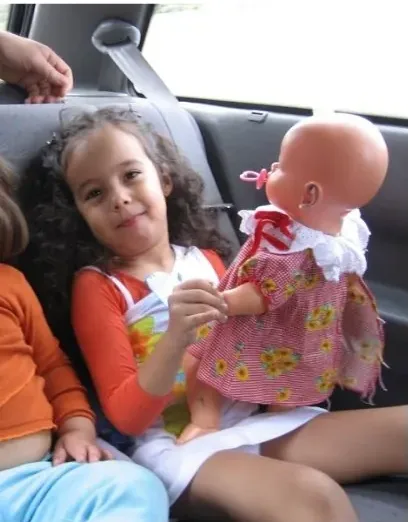 Mariana criança sentada no carro segurando uma boneca