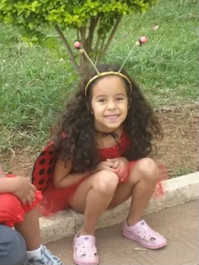 Mariana criança agachada na grama com uma tiara de anteninhas